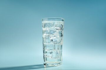 Soda water with ice cubes in glass on light blue background