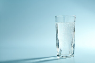 Soda water in glass on light blue background, space for text