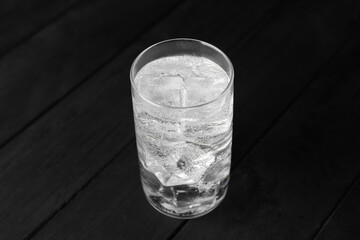 Refreshing soda water with ice cubes in glass on black wooden table, closeup