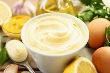 Delicious mayonnaise sauce in bowl and ingredients on table, closeup
