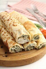 Tasty rolled crepes with cottage cheese and spinach served on white wooden table, closeup