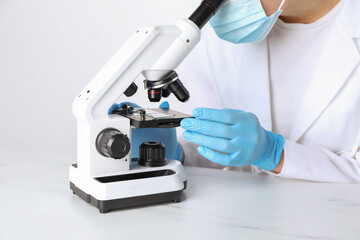 Laboratory testing. Scientist working with microscope at white marble table, closeup
