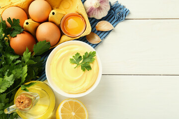 Delicious mayonnaise sauce with parsley in bowl and ingredients on white wooden table, flat lay. Space for text