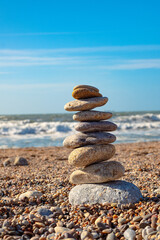 Beautiful installation of sea stones on the beach. A tower of pebbles stands on a beach sand against the backdrop of the ocean