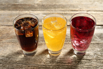 Soda water of different flavors with ice cubes in glasses on wooden table, closeup