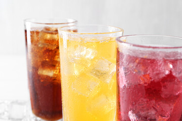 Soda water of different flavors with ice cubes in glasses on white table, closeup
