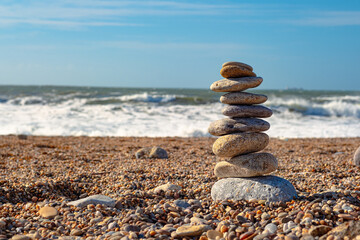 Beautiful installation of sea stones on the beach. A tower of pebbles stands on a large stone against the backdrop of the ocean