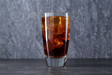 Sweet soda water with ice cubes in glass on grey table