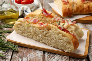 Slices of delicious focaccia bread with bacon and rosemary on wooden table, closeup