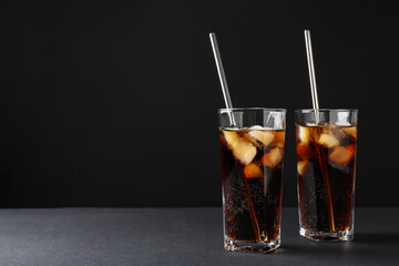 Refreshing cola with ice cubes and drinking straws in glasses on black table, space for text