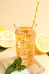 Refreshing iced tea with drinking straw in glass, mint and lemon on beige background, closeup