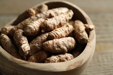 Raw turmeric roots in bowl on wooden table, closeup