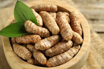 Tumeric rhizomes with leaves in bowl on table, closeup