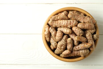 Tumeric rhizomes in bowl on white wooden table, top view. Space for text