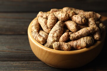 Tumeric rhizomes in bowl on wooden table, closeup