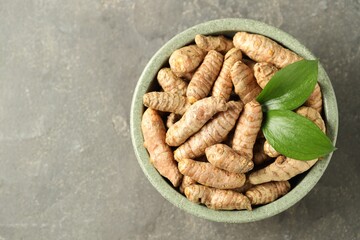 Tumeric rhizomes with leaves in bowl on grey table, top view. Space for text