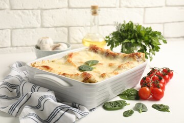 Delicious spinach lasagna in baking dish and ingredients on white table