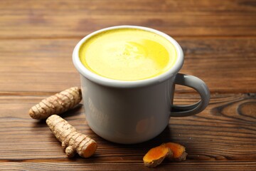 Tasty turmeric latte in cup and roots on wooden table, closeup