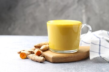 Tasty turmeric latte in cup and roots on grey table, closeup