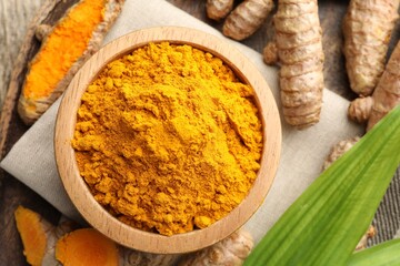 Turmeric powder in bowl, roots and leaves on table, flat lay