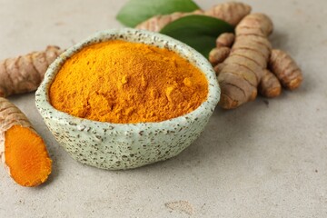 Aromatic turmeric powder in bowl, fresh roots and leaves on light grey table, closeup