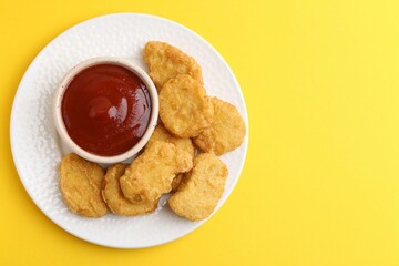 Tasty chicken nuggets with sauce on yellow background, top view. Space for text