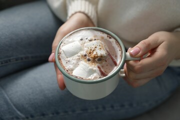 Woman holding mug of tasty hot chocolate with marshmallows and cinnamon on sofa, closeup