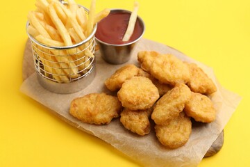 Tasty chicken nuggets, potato fries and sauce on yellow background, closeup