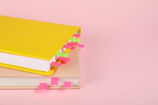 Books with colorful tabs on pink background, closeup. Space for text