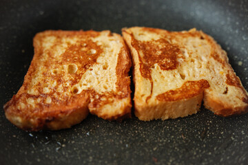 Close-up of two nicely golden pieces of French toast cooking in a frying pan, preparing traditional breakfast