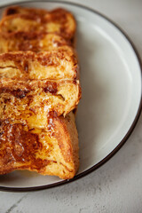 Close-up of French toast with honey, traditional sweet homemade breakfast of bread soaked in eggs and milk, served on a white plate and shot in bright morning light with copy space on right side