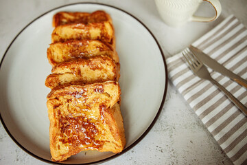 French toast with honey, traditional sweet homemade breakfast of bread soaked in eggs and milk, served on a white plate and shot in bright morning light with copy space on right side