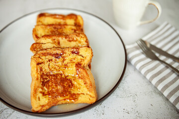 French toast with honey, traditional sweet homemade breakfast of bread soaked in eggs and milk, served on a white plate and shot in bright morning light with copy space on right side