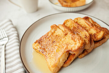French toast with honey, traditional sweet homemade breakfast of bread soaked in eggs and milk, served on a white plate and shot in bright morning light with copy space
