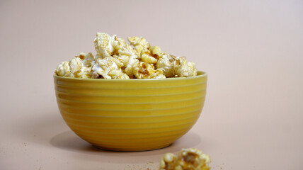Popcorn bowl placed on beige background. Front view popcorn in yellow bowl with copy space. Concept of ceramic tableware, delicious, tasty, and crispy texture. Sweet popcorn for snack time at home.