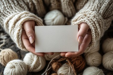 Woman wearing knitted sweater holding blank business card surrounded by yarn balls, perfect for knitters, crafters, and small business owners