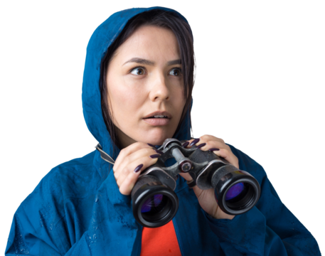 A tourist girl in a blue raincoat holds binoculars in her hands and looks into the distance, spies.