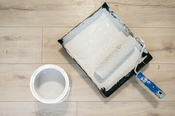Top view of paint roller with blue handle in tray of gray paint  and can of gray paint on natural wooden background