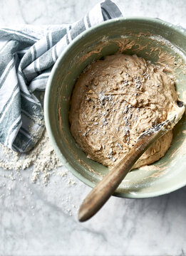 Stirring sourdough bread dough with a wooden spoon in a ceramic bowl, vertical close-up.