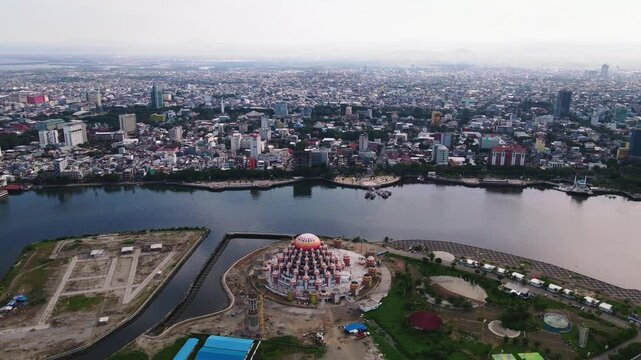 The atmosphere of the construction of Losari Beach and the 99-dome mosque with the backdrop of the cityscape on a sunny day and clear sea.