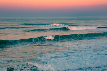 The most beautiful sunrise on the ocean coast. Golden hour on the beach. The sky in bright pink and blue colours of dawn and big beautiful ocean waves with white caps on the crests