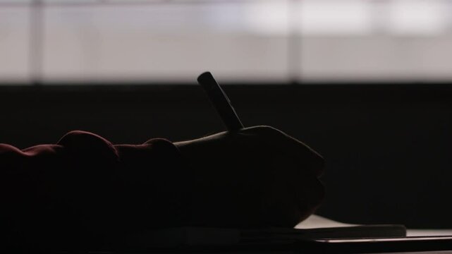 dimly lit scene of a hand is writing, leaving the pen and picking phone, started to scroll