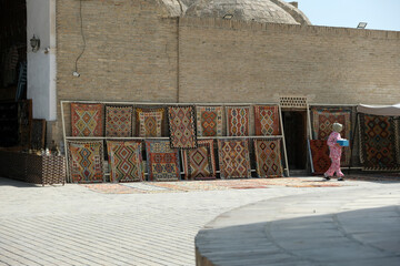 traditional Uzbek carpets are hung along the brick wall of a building, Bukhara