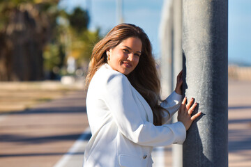 Young and beautiful blonde woman rests her hands on a lamppost and looks at the camera very happy...