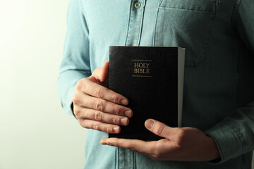 Man with hardcover Holy Bible on light background, closeup. Space for text