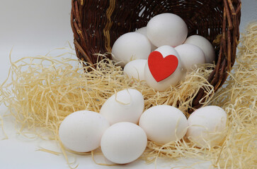 White eggs rolling out of a wicker basket, one egg is decorated with a red heart, we love Easter