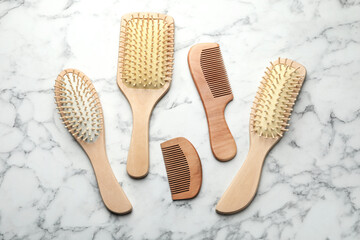 Wooden hair brushes and combs on white marble background, flat lay