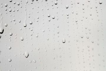 Water drops on light grey glass surface, closeup