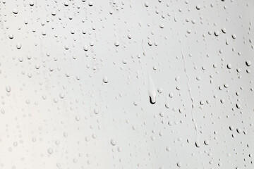 Water drops on light grey glass surface, closeup