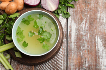 Tasty chicken bouillon in bowl and ingredients on wooden table, flat lay. Space for text